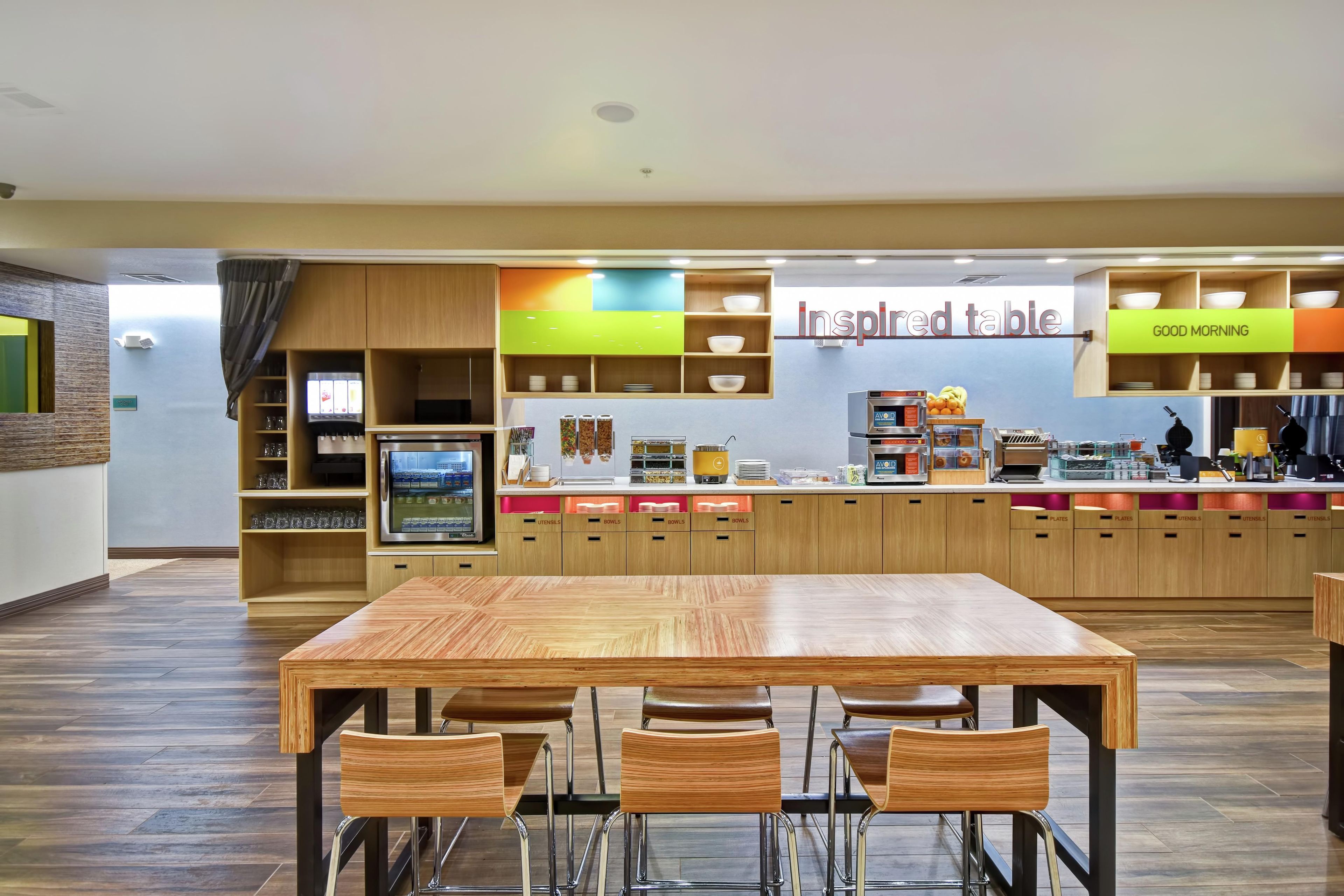 A restaurant with a wooden table and chairs, a counter with a menu, and a sign that reads 'inspired table'.