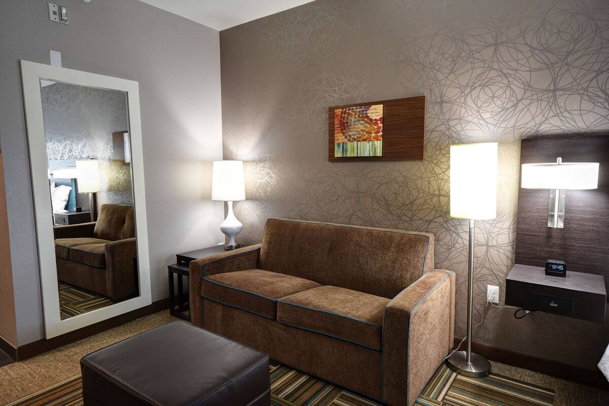 A hotel room with a sofa, a mirror, a lamp, a clock, and a wall with a textured pattern.