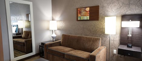 A hotel room with a sofa, a table, a lamp, a painting, and a mirror.