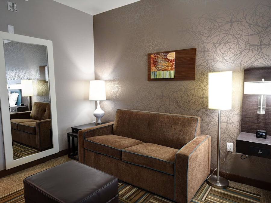 Una habitación de hotel con sofá, una mesa, una lámpara, un cuadro y un espejo.