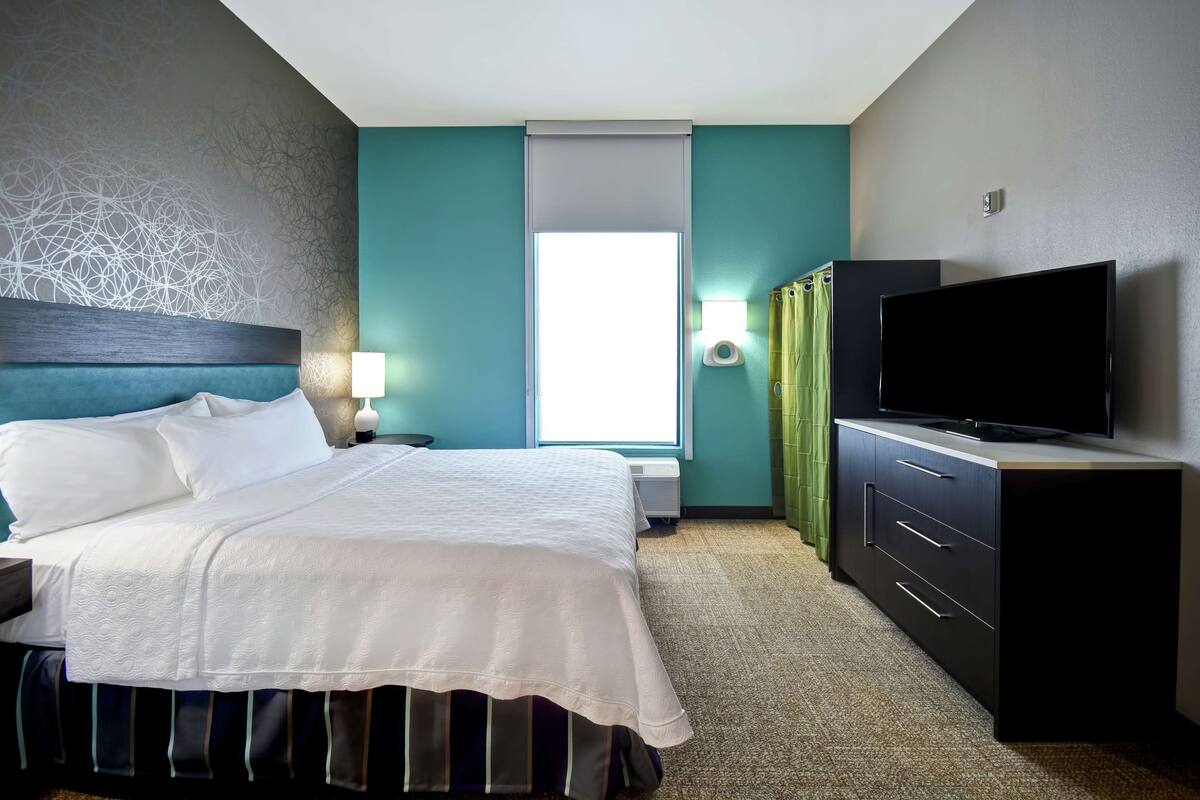 A hotel room with a bed, a TV, a desk, and a window.