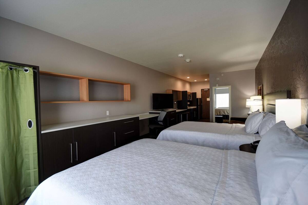 A hotel room with two beds, a desk, a TV, and a bathroom.
