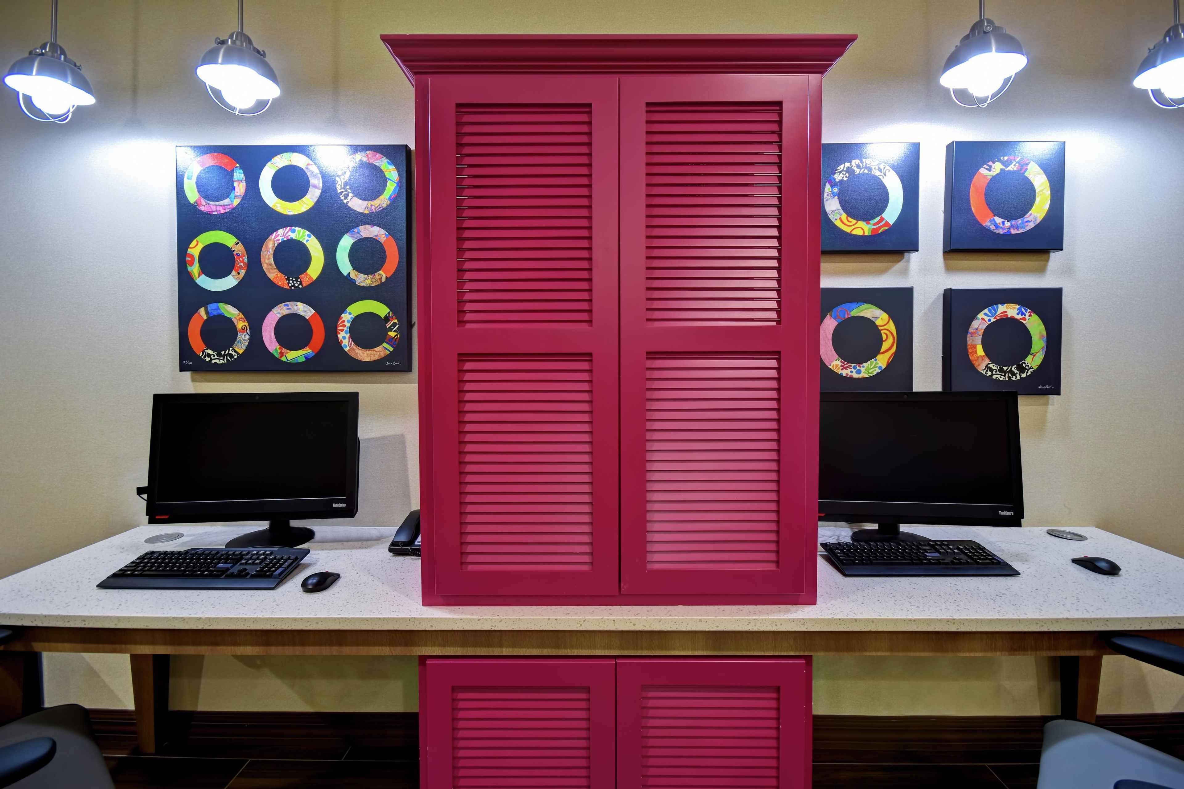 Un espacio de trabajo con dos monitores, un teclado, un ratón y un armario rojo con puertas persianas.