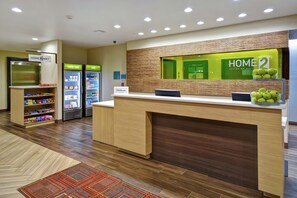 Un espace d’accueil d’hôtel comprenant un comptoir, des distributeurs automatiques et une présentation de pommes vertes.