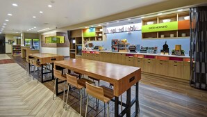 Um restaurante moderno com mesas e cadeiras de madeira, um balcão com a placa 'Good Morning' e a placa 'Inspired Table'.