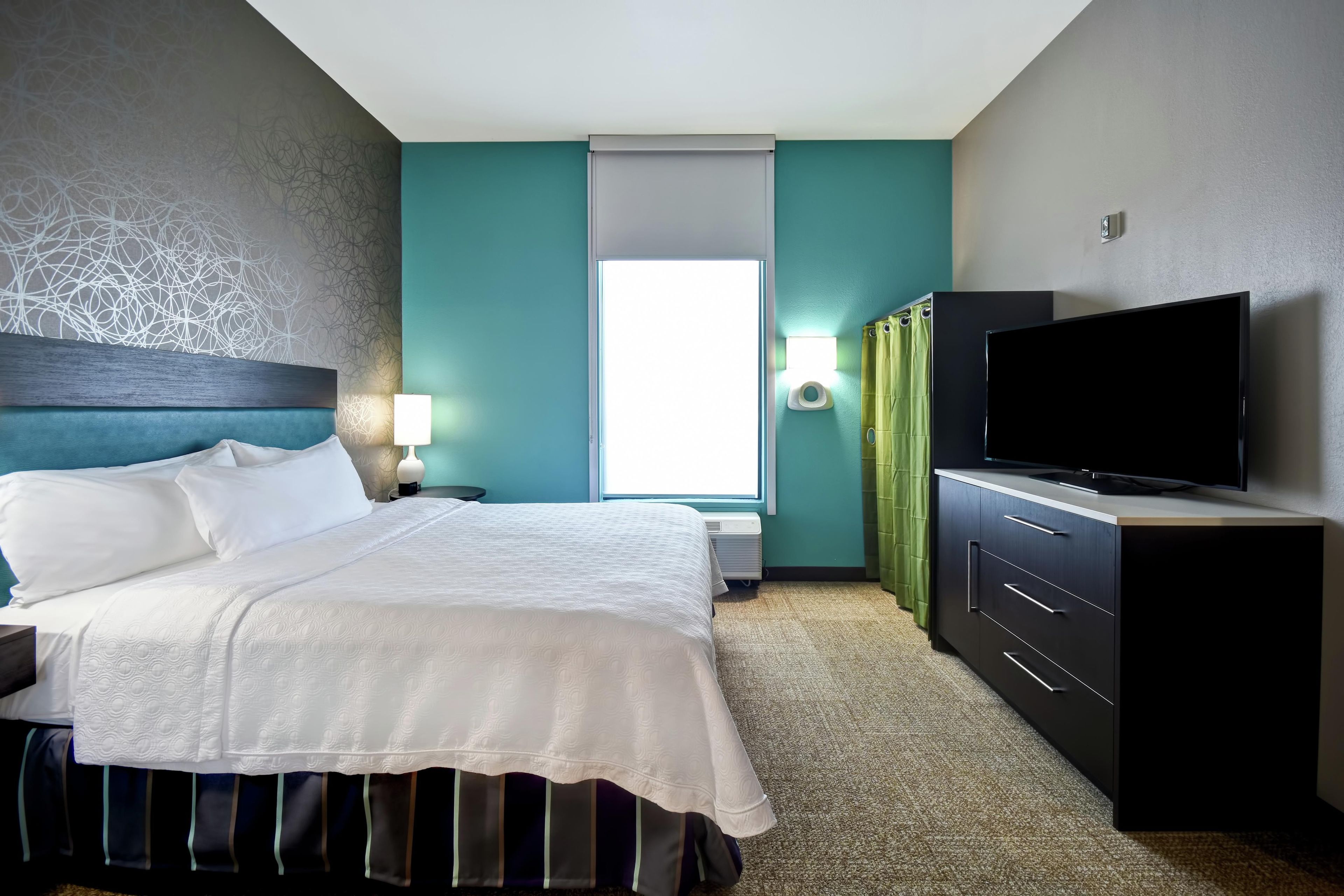A hotel room with a bed, a flat-screen TV, a desk, and a window.
