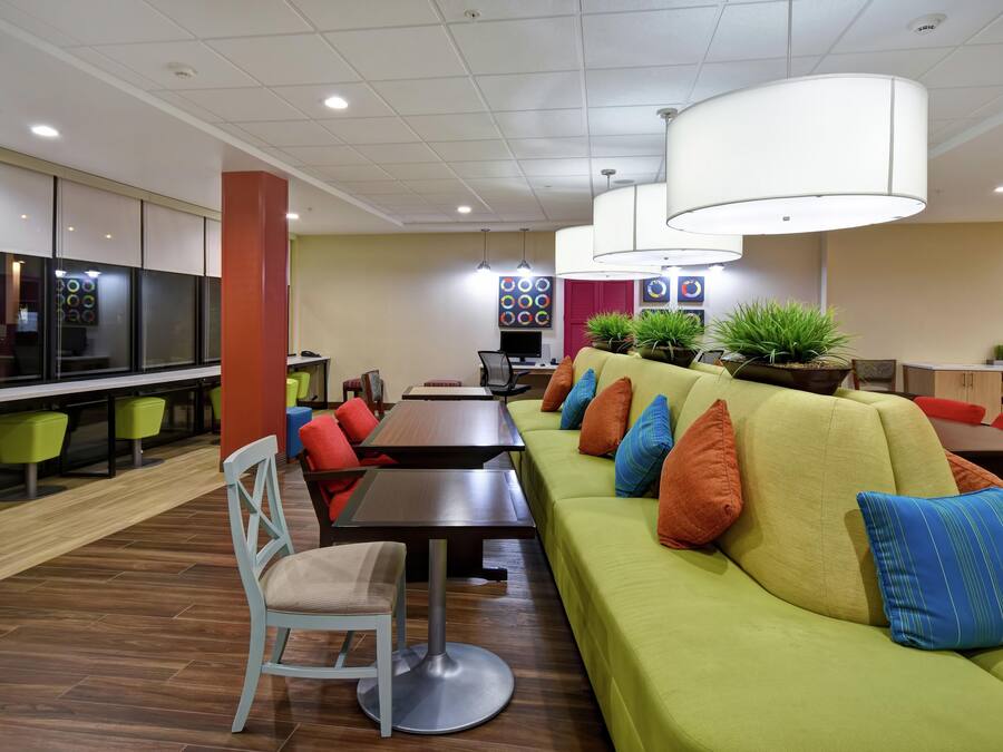 A modern lounge area with a green sofa, wooden tables, and colorful chairs.