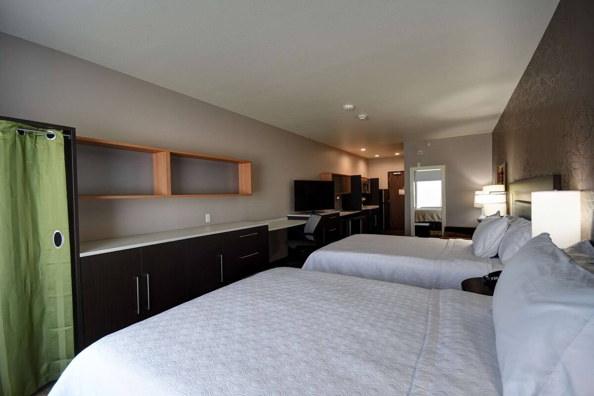 A hotel room with two beds, a desk, a TV, and a bathroom with a shower curtain.