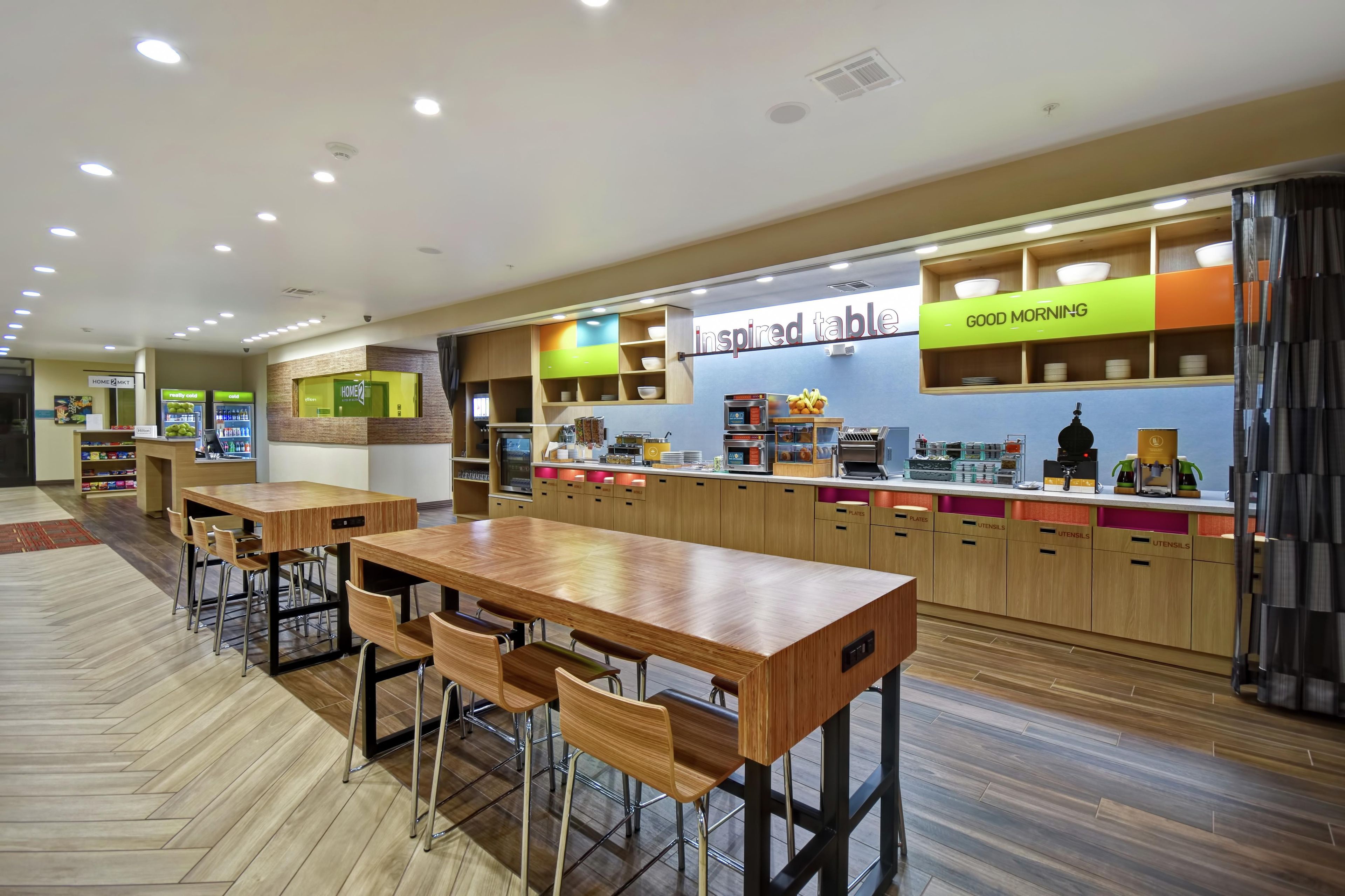 A modern restaurant with wooden tables and chairs, a counter with a 'Good Morning' sign, and a 'Inspired Table' sign above the counter.
