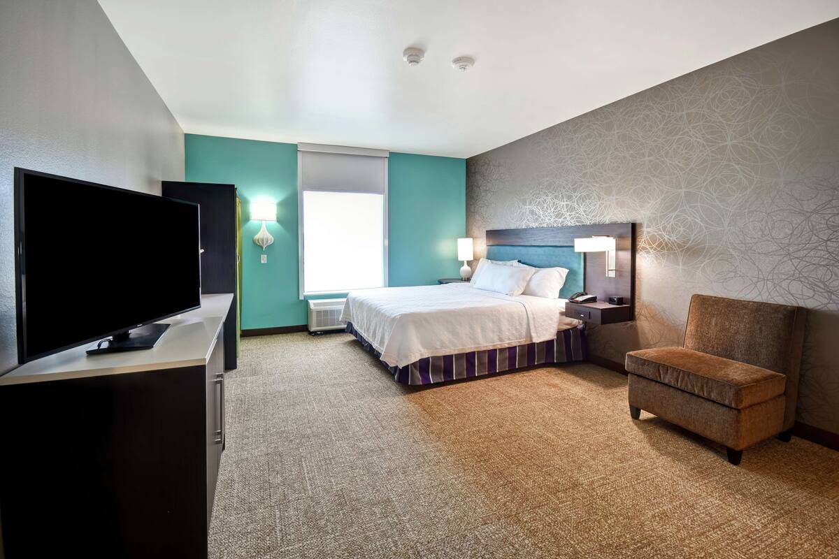 A hotel room with a bed, a TV, a chair, and a desk.