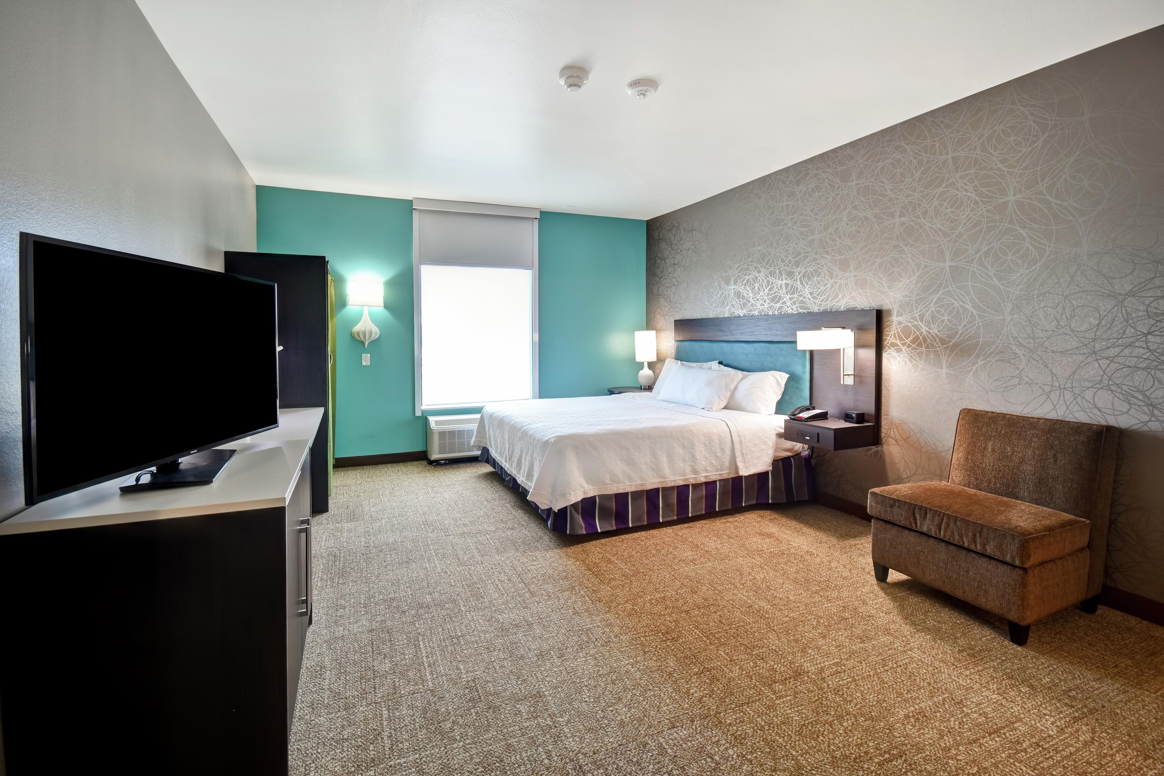 A hotel room with a bed, a TV, a chair, a desk, and a window.