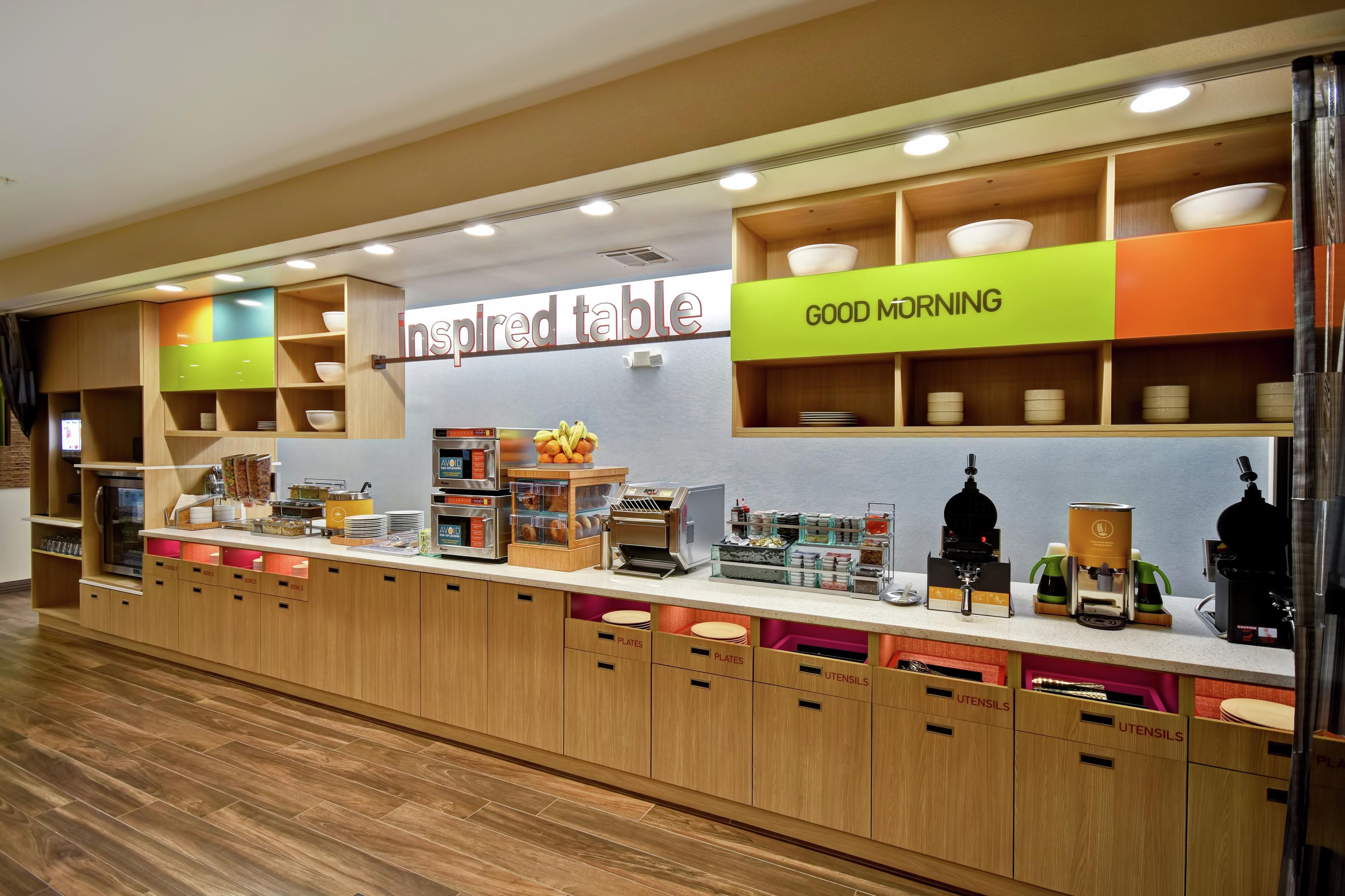 A breakfast buffet area with labeled sections for bowls, plates, and utensils.