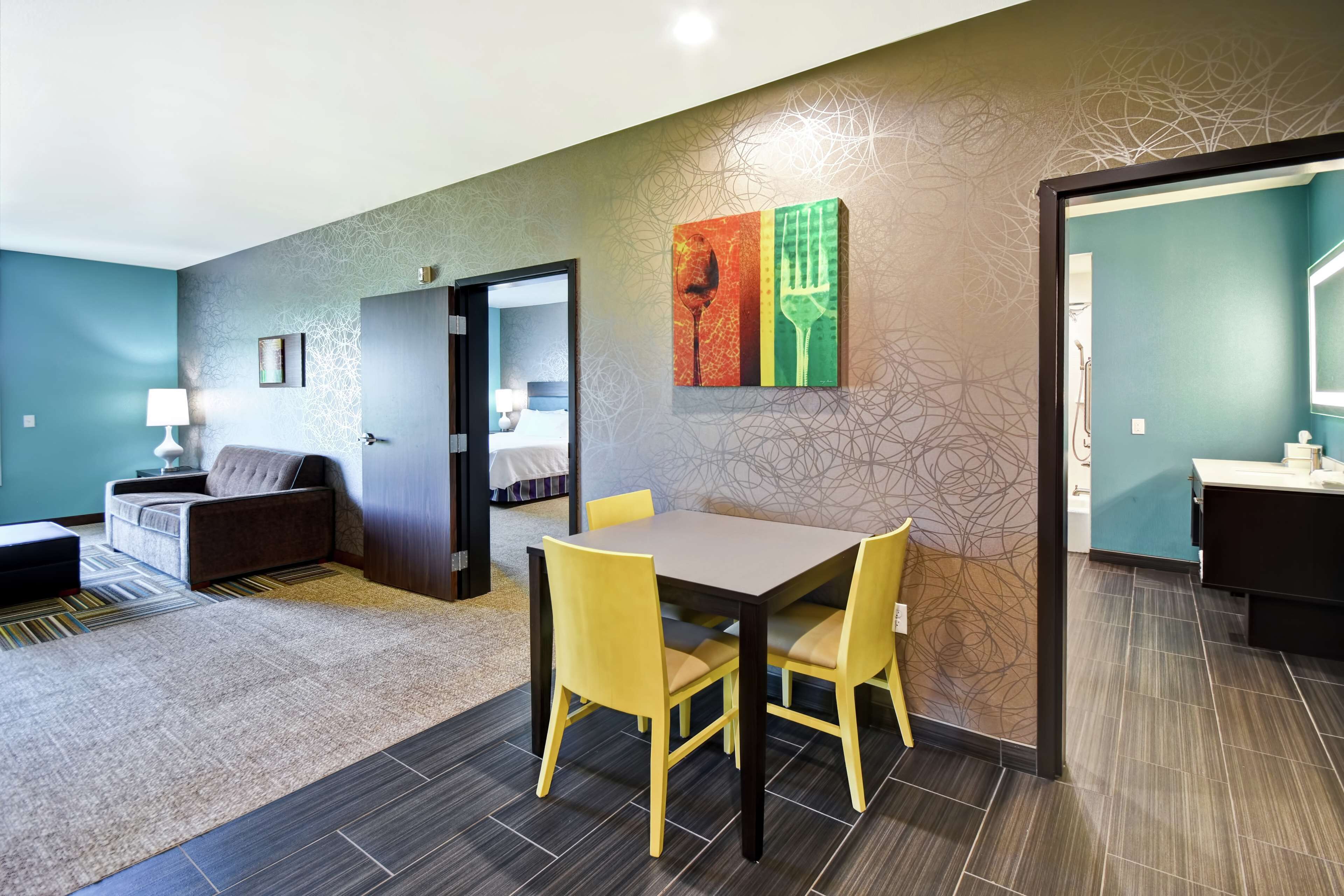 A modern hotel room with a dining area, a sofa, a lamp, and a painting on the wall.