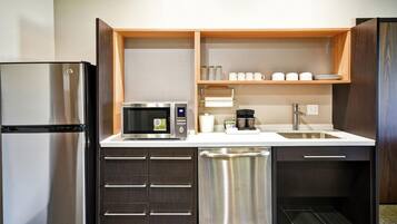 A compact kitchen with a refrigerator, microwave, coffee maker, and a dishwasher.