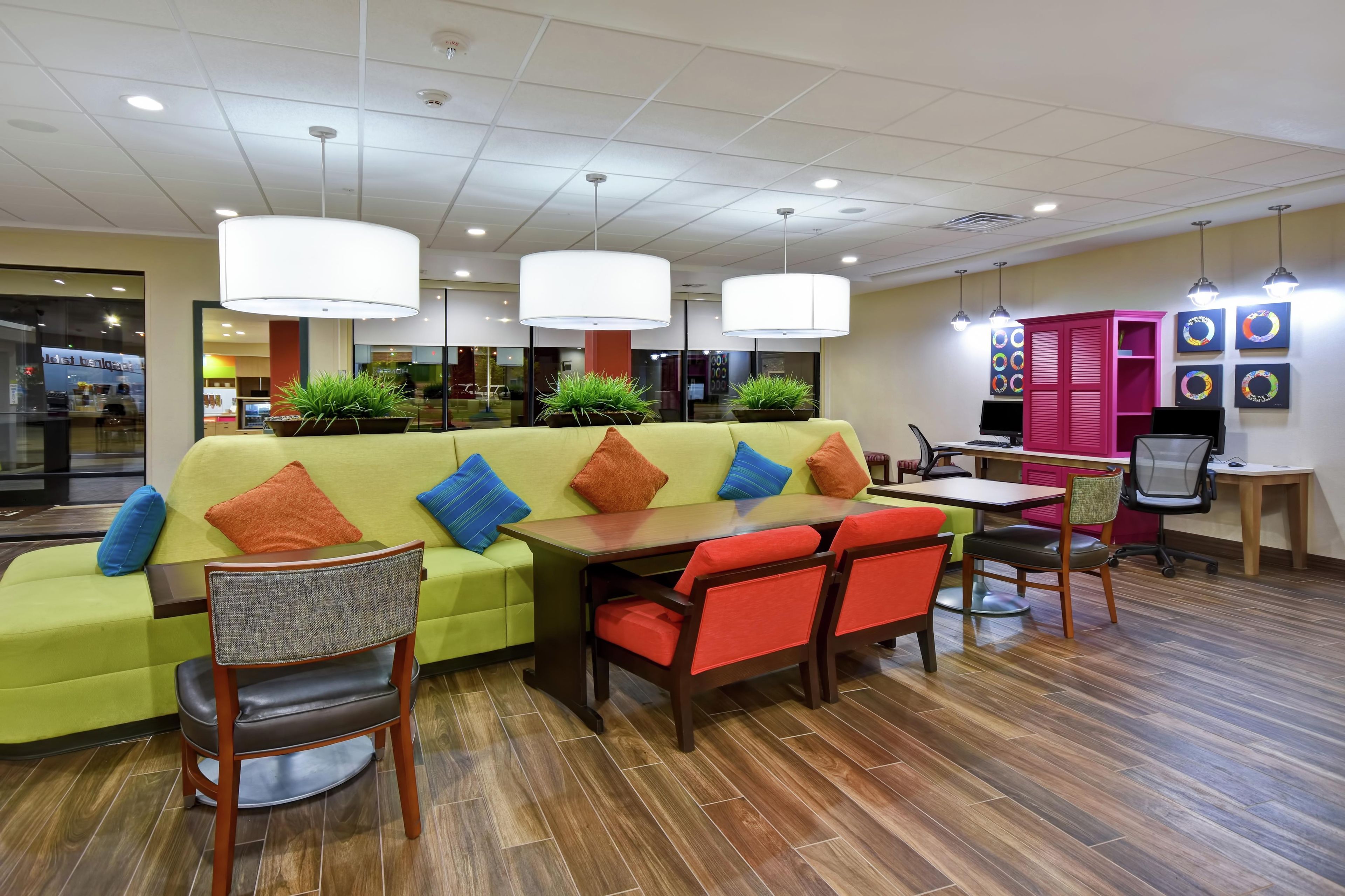 A modern interior with a green sofa, wooden chairs, a dining table, and pendant lighting.