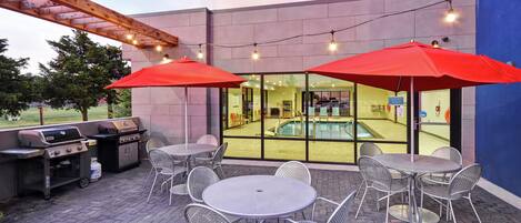 An outdoor patio with metal tables and chairs, a barbecue grill, and a swimming pool visible through the glass doors.