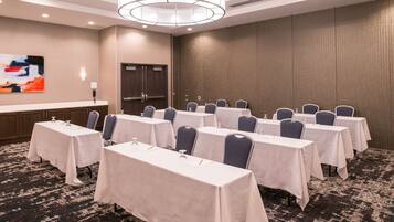 Un salón de conferencias con varias mesas y sillas, una lámpara de araña grande y una obra de arte colgada en la pared.