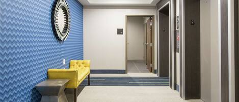 Un vestíbulo de hotel con una pared de diseño azul, un sofá amarillo, un espejo moderno y suelo alfombrado.