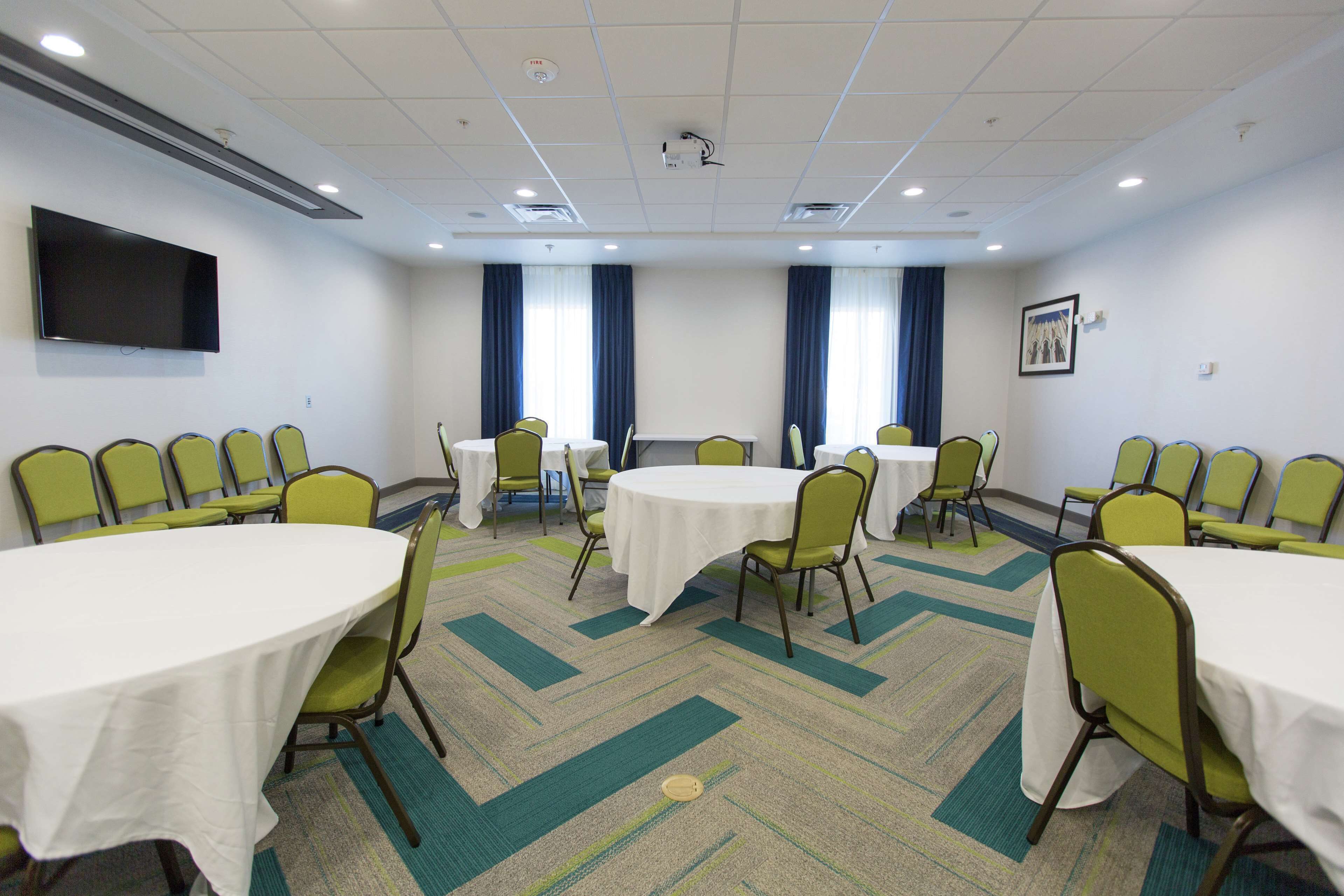 A conference room with multiple tables and chairs, a flat-screen TV, and large windows with blue curtains.