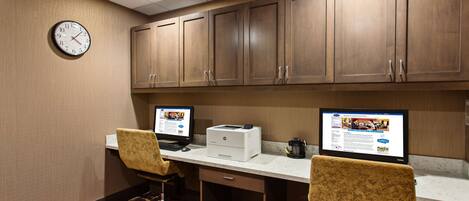 A hotel room with a desk, two chairs, a clock, and wooden cabinets.