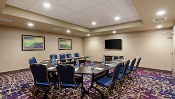 A conference room with a large table, blue chairs, water bottles, and a flat-screen TV on the wall.