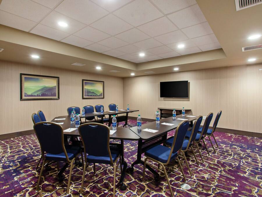 A conference room with a large table, blue chairs, water bottles, and a flat-screen TV on the wall.