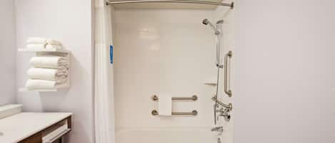 A modern bathroom with a bathtub, a toilet, and a sink. There are towels on a shelf and a shower curtain.