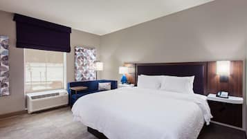 A hotel room with a large bed, a bedside table with a lamp, a wall-mounted phone, and a window with a view.