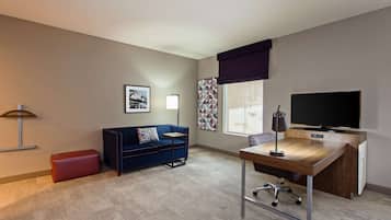 A modern room with a blue sofa, a wooden desk, a television, and a window with patterned curtains.
