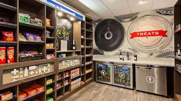 Zona de exhibición de bocadillos y bebidas con estantes llenos de diversas opciones, un refrigerador y una pared con el letrero 'Treats'.