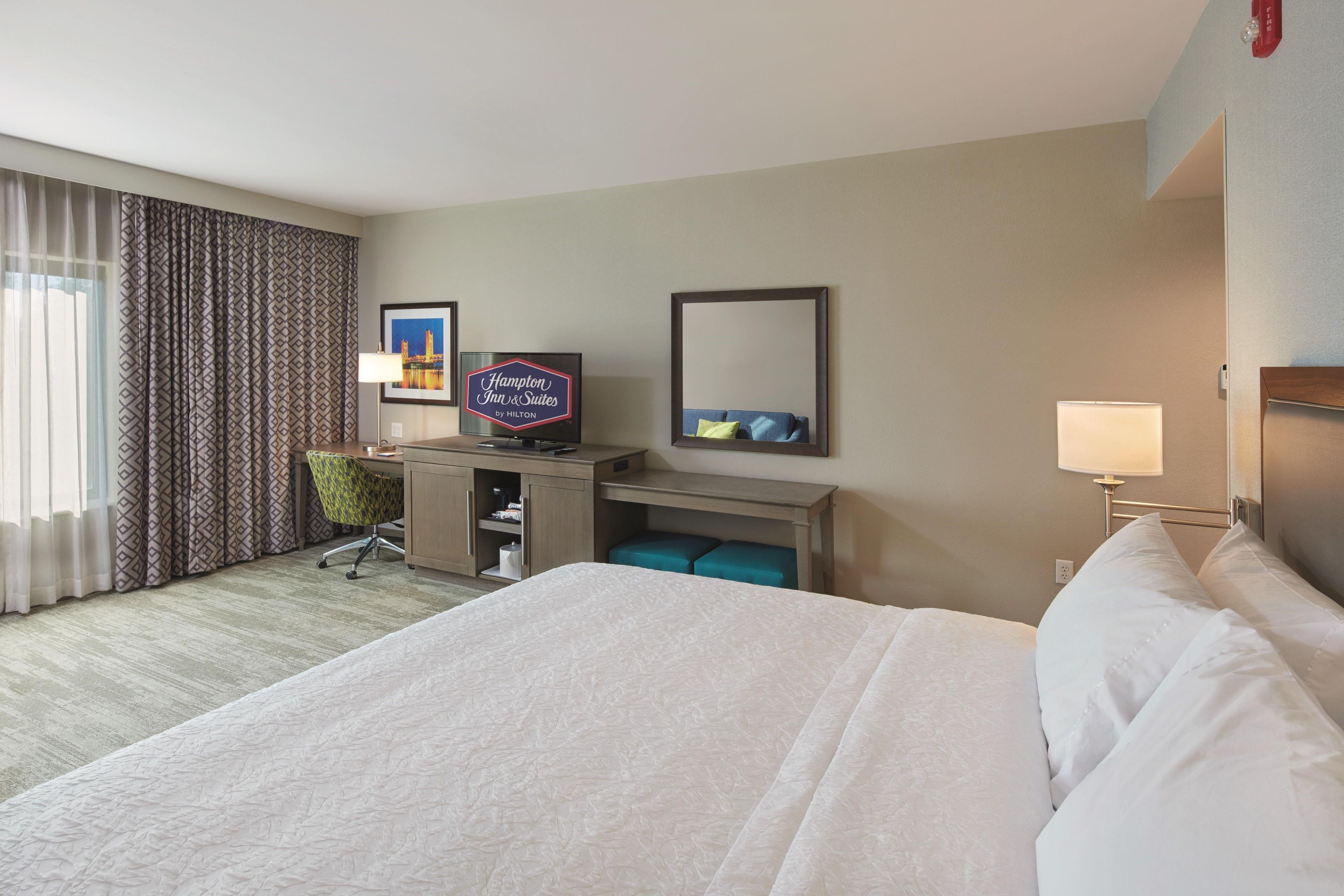 A hotel room with a large bed, a desk with a computer, a chair, a television, and a mirror.