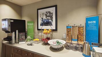 Zona de buffet per esmorzar amb màquina de cafè, fruita i cereals, i diverses salses.