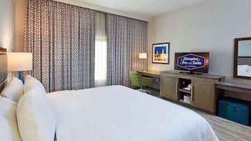 Une chambre d’hôtel avec un grand lit, un bureau avec une télévision, des rideaux à motifs et une enseigne « Hampton Inn & Suites ».