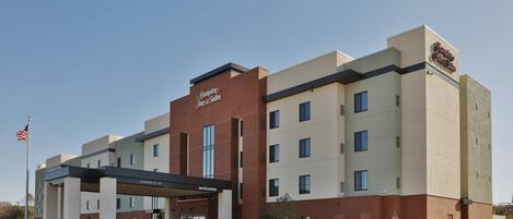 A Hampton Inn & Suites hotel with a modern facade, a covered entrance, and a clear sky.