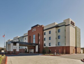 Een Hampton Inn & Suites hotel met een moderne gevel, een overdekte ingang en een heldere lucht.