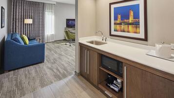 Een moderne hotelkamer met een kitchenette, een bank, een televisie en een schilderij van een brug.