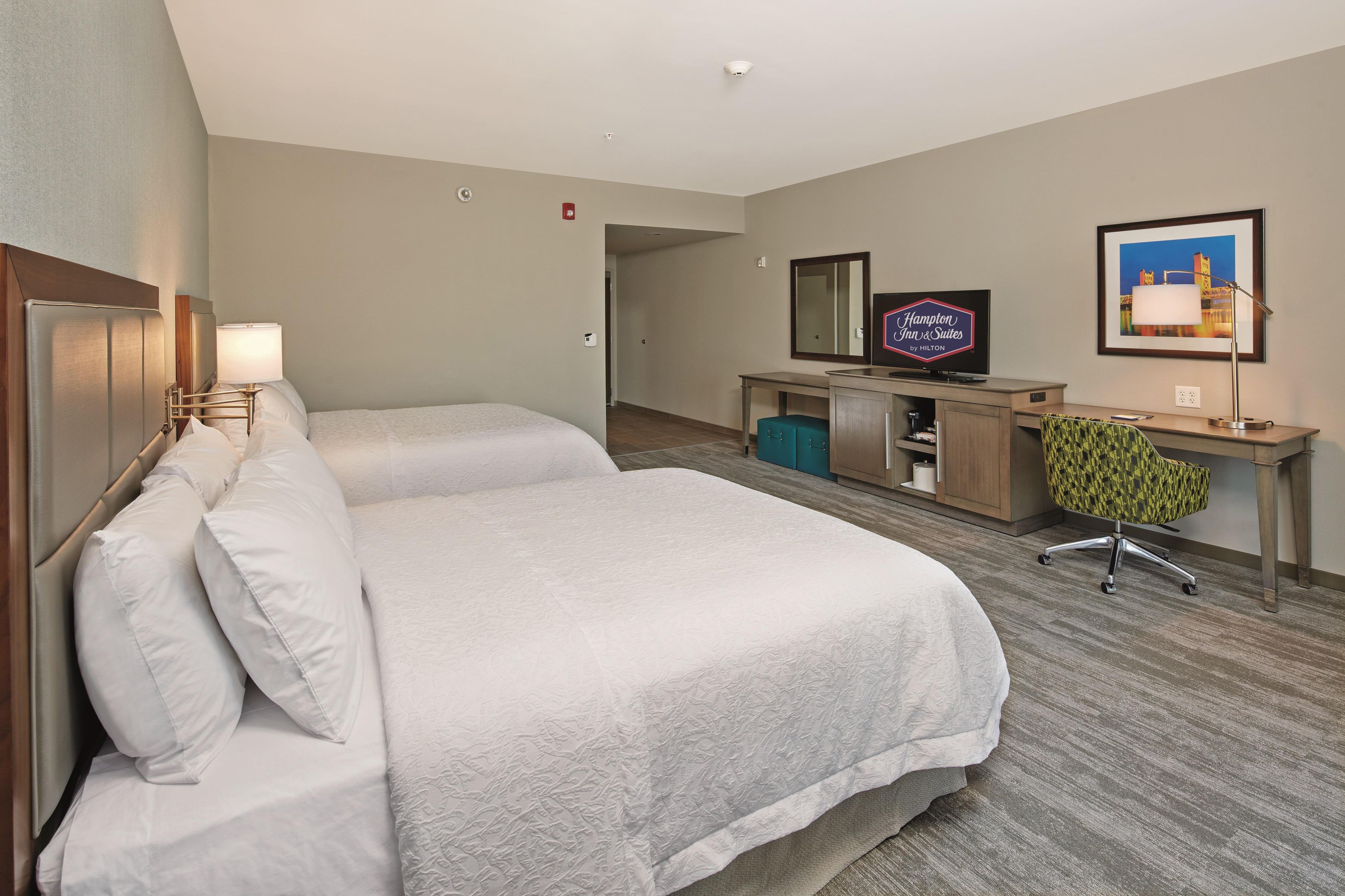 A hotel room with a double bed, a desk with a television, a chair, and a framed picture on the wall.