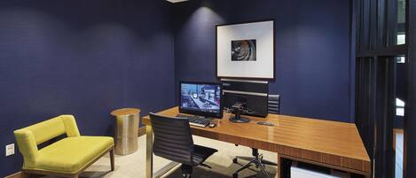 Ein moderner Arbeitsraum mit Schreibtisch aus Holz, zwei Stühlen, einem Computerarbeitsplatz und einem gerahmten Bild an der Wand.