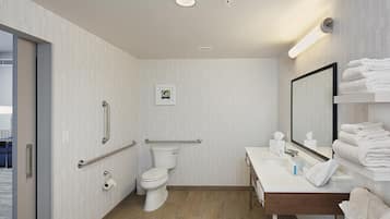 A modern bathroom with a toilet, bidet, handrails, a sink with a mirror, and a towel rack.