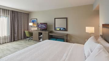 Habitación de hotel con una cama grande, un escritorio con computadora, una silla, un televisor y un cartel de Hampton Inn & Suites by Hilton.