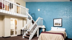 A bedroom with a bed, a nightstand, a lamp, a framed picture on the wall, and a staircase leading to an upper level. - Motel 6 Tallahassee, FL – North Monroe (Tallahassee)