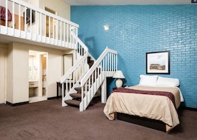 Un dormitorio con cama, mesita de noche, lámpara, un cuadro enmarcado en la pared y una escalera que sube a un nivel superior.
