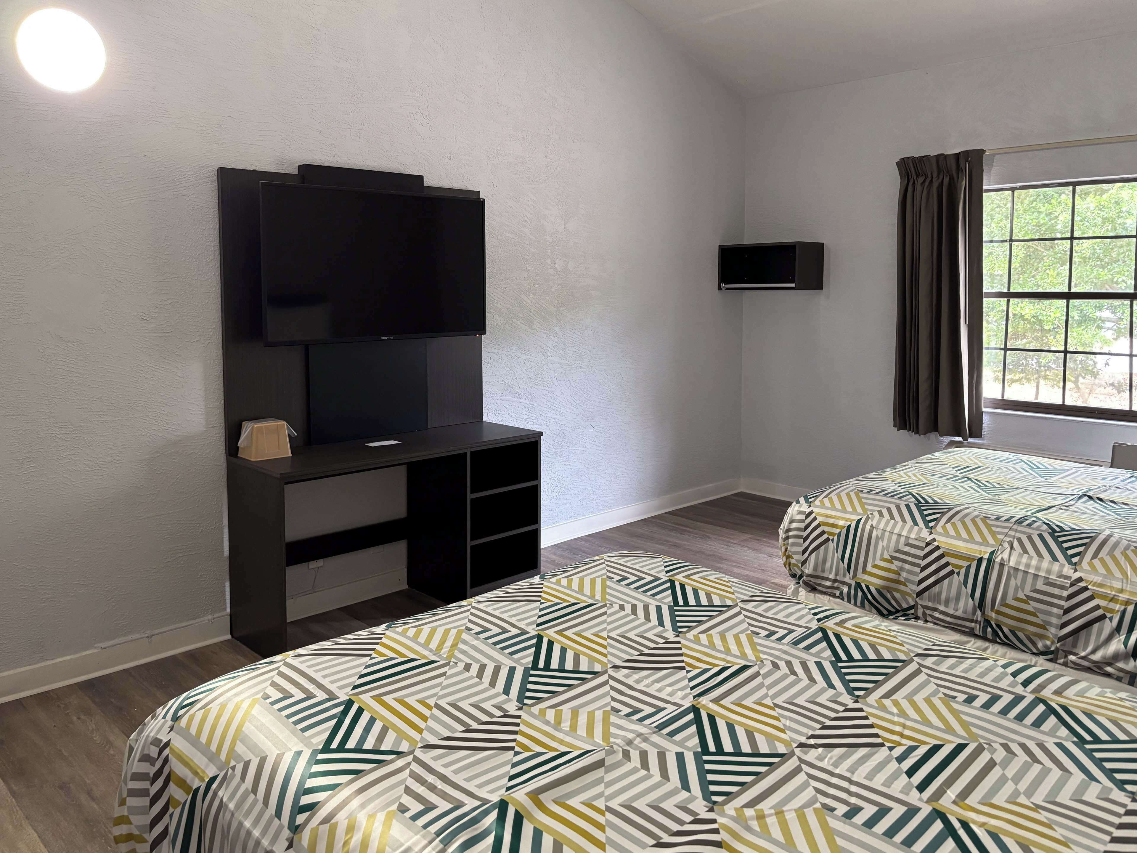 A hotel room with a bed, a TV, a small desk, and a window with curtains.