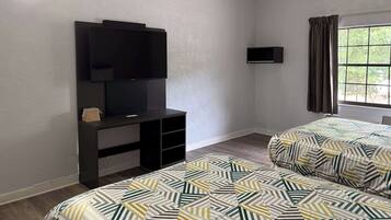 A hotel room with a bed, a TV, a small desk, and a window with curtains.