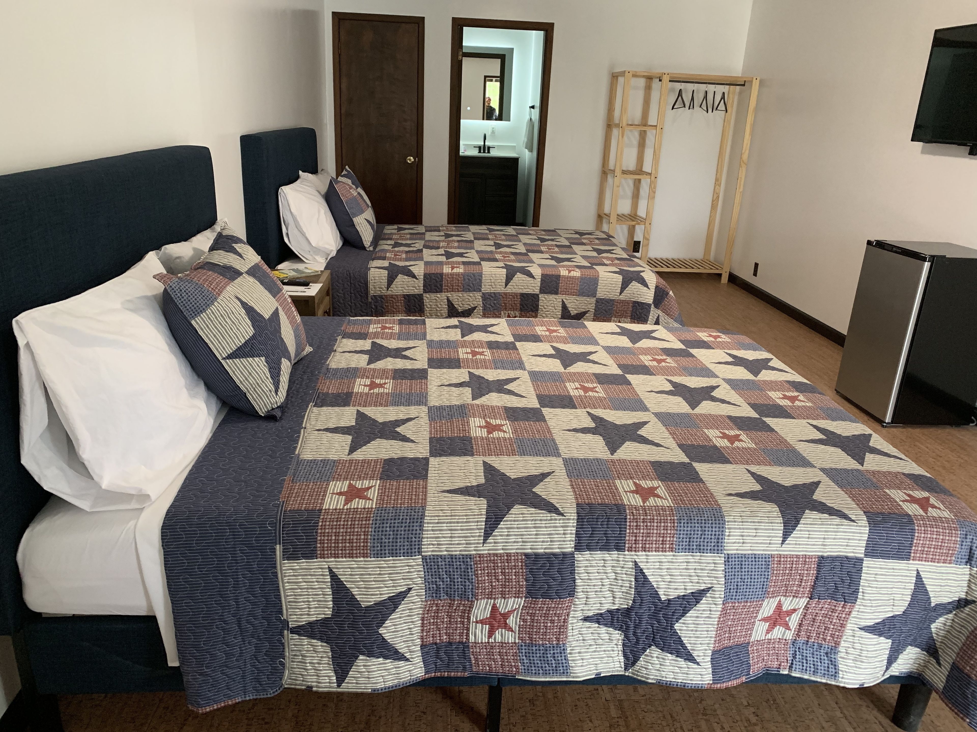 A hotel room with two beds, a wooden wardrobe, a television, and a refrigerator.
