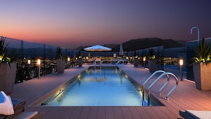 A rooftop pool area with a clear view of the cityscape at dusk, equipped with lounge chairs and umbrellas. - Zip Housing El Golf (Santiago)