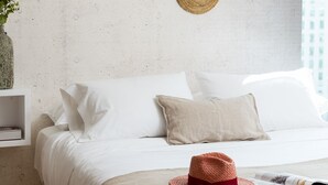 A neatly made bed with white bedding, a red woven hat, and a magazine on a beige throw. - Zip Housing El Golf (Santiago)