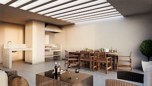 A modern outdoor dining area with a high ceiling and skylight, wooden furniture, and a small table with wine bottles. - Zip Housing El Golf (Santiago)