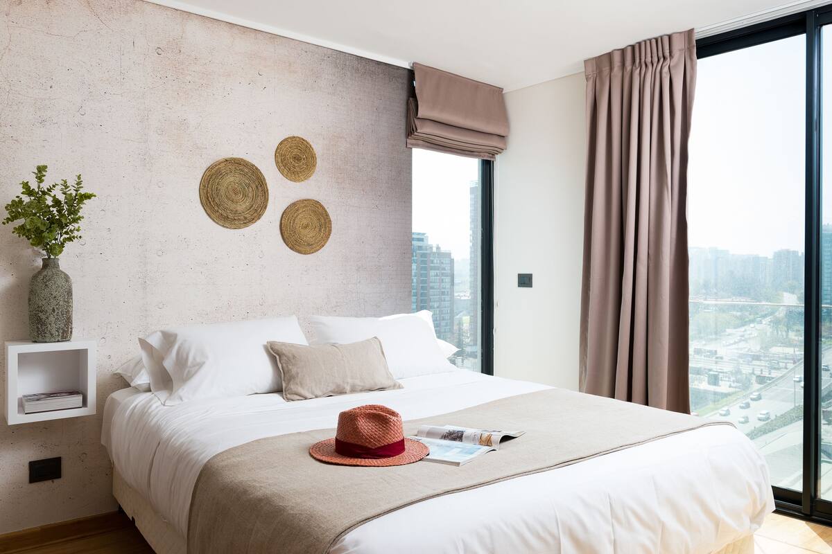 A modern hotel room with a large bed, a view of the city, and a decorative wall with woven circles.