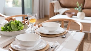 A dining table set with white plates, bowls, and cutlery, with a bowl of green salad and a glass of water. - Zip Housing El Golf (Santiago)
